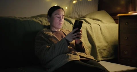 Woman using a smartphone while sitting on the floor in her bedroom at night. Stock Footage 328727874
