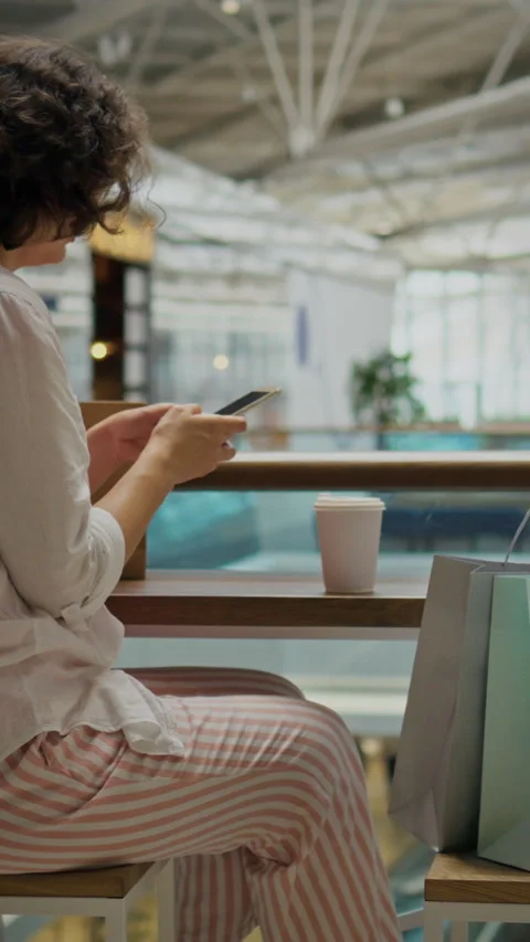 Woman using smartphone while sitting at a table in a modern cafe during dayt Stock Footage 331739861