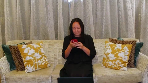 Woman using smartphone while sitting on sofa at home Stock Footage 341423976