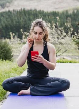 Woman using smartphone while sitting on yoga mat, copy space. Stock Photos