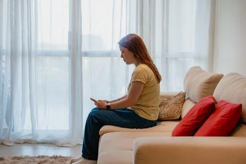 Woman using smartphone while sitting on a sofa at home Stock Photos