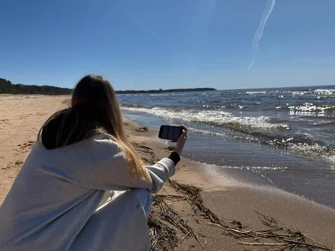 Woman Using Smartphone While Sitting on Sunny Beach Shore Photos