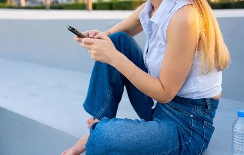 Woman using smartphone while sitting outdoors on modern urban steps in casual Stock Photos