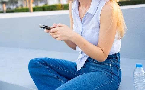 Woman using smartphone while sitting on urban pavement in casual style Stock Photos
