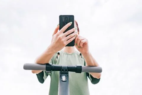 Woman using smartphone while standing with an e-scooter outdoor. Stock Photos