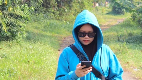 Woman using a smartphone while walking along a rural path Stock Footage 337275470