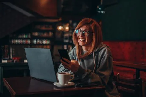 Woman using a smartphone while working on her laptop in a cafe Stock Photos