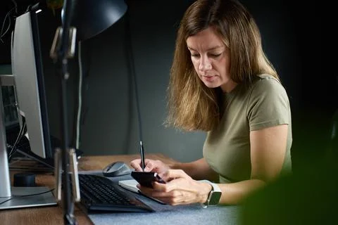 Woman using smartphone while working at home office desk Stock Photos