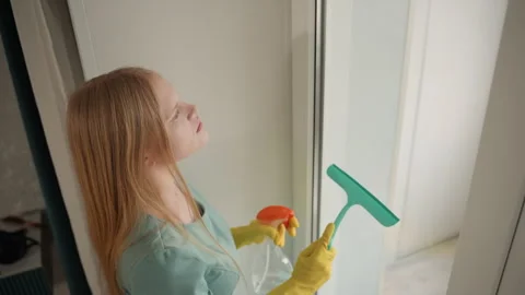 Woman using squeegee and spray in welllit modern home. Young woman meticulously Stock Footage 336864681