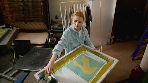 Woman Using Squeegee on Screen Printing Frame in Workshop Video stock 333162143