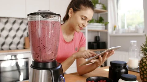 Woman using a tablet and preparing smoothie at kitchen Stock Footage 93342449