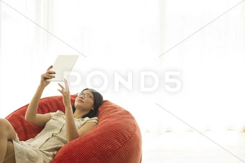 Woman using tablet computer in beanbag chair Stock Photos
