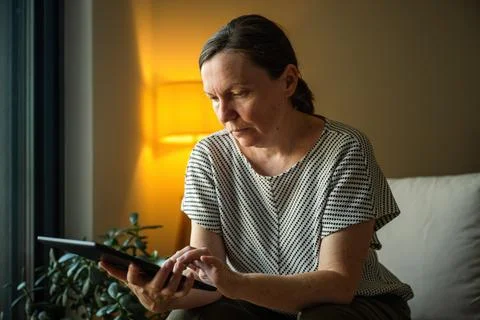 Woman using a tablet computer in a comfortable home setting during the even.. Stock Photos