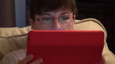 Woman using a tablet computer on a couch at home, reflection in glasses Stock Footage 33796969