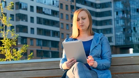 Woman using tablet computer sitting on bench in city Stockbeeldmateriaal 111003217