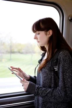Woman using tablet computer while standing by window in train Stock Photos