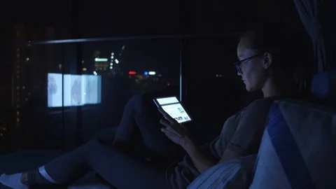 Woman using the tablet pc and sitting beside the window. Tv light on mirror Stock Footage 88099855