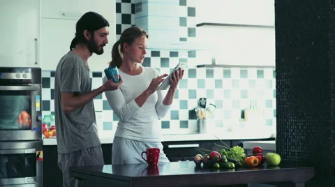 Woman using a tablet standing at the kitchen with man holding a cup Stock Footage 56966583