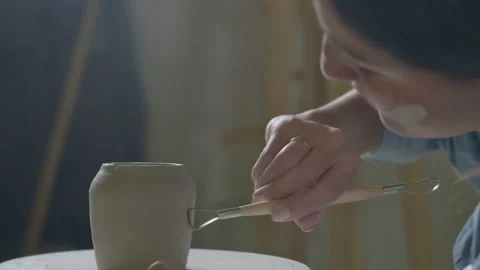 A woman using tools to make a ceramic clay cup handle in a pottery workshop Stock Footage 233296998