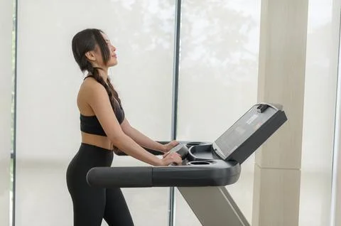 Woman Using Treadmill Machine in Modern Gym with Large Windows Stockfoto's