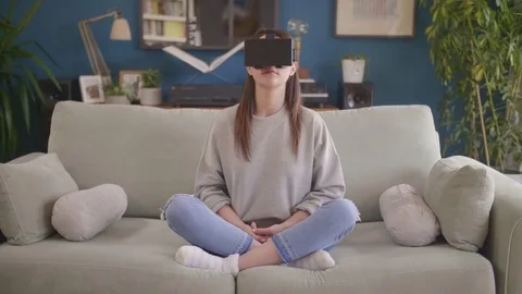 Woman using virtual reality simulator while performing yoga on sofa Stock Footage 79658873