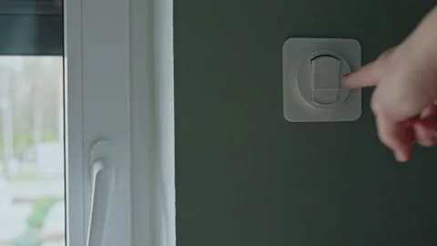 Woman using wall control to lower exterior roller shutter beside window 库存影片 332076647