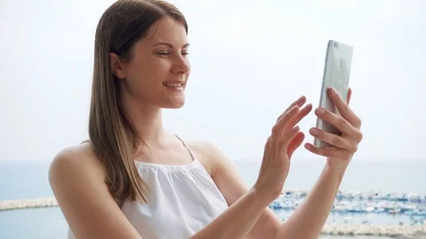 Woman on vacation having video chat with friend on balcony via mobile messenger Stock Footage 89942013