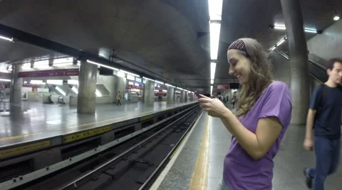 A woman waiting for a train, while she typing some message in your smartphone Видео 57829011