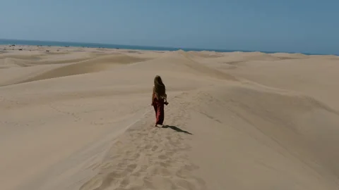 Woman walking across endless sand dunes under a clear blue sky. Scenic desert Stock Footage 338317446