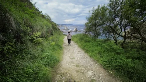 Woman walking alone on a path towards the beach Видео 336112060