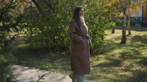 Woman walking along paved path in sunlit urban park with autumn foliage close up Stock Footage 346662531