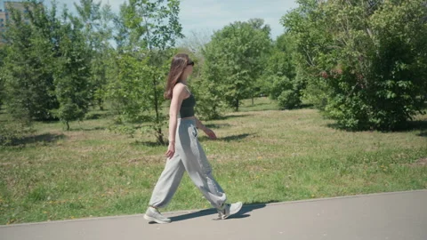Woman walking along tree lined path in outdoor park with green foliage and Stock Footage 345135156