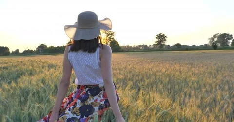 A woman is walking along a wheat field with a white dress, in a straw hat Stock Footage
