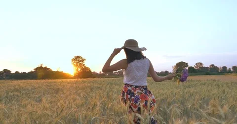 A woman is walking along a wheat field with a white dress, in a straw hat Stock Footage