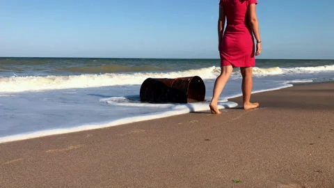 Woman walking on the beach near a rusty barrel Stock Footage