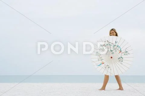 Woman Walking Behind Parasol At The Beach, Smiling At Camera