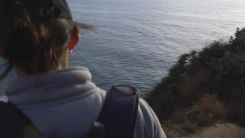 Woman walking down a path, overlooking ocean from a cliff, 4k Stock Footage 103437515
