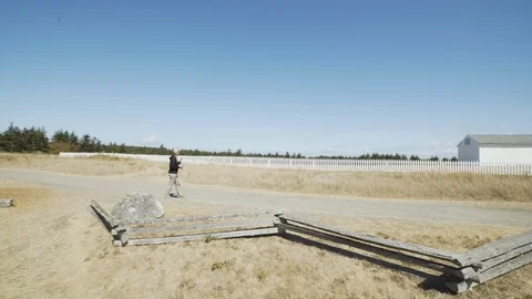 Woman walking down path past white buildings in park on northwest island Stock Footage 100560762