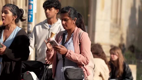 A woman walking down a street using her phone while eating ice cream Stock Footage 279560740