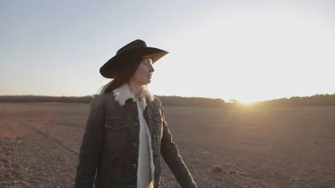 Woman walking on empty field at sunset wearing cawboy hat and jeans coat Stock Footage 127720344