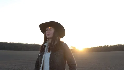 Woman walking on empty field at sunset wearing cawboy hat and jeans coat Stock Footage 127720751