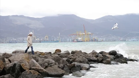 Woman is walking by empty seafront in windy weather with crashing sea waves Stock Footage 125112172