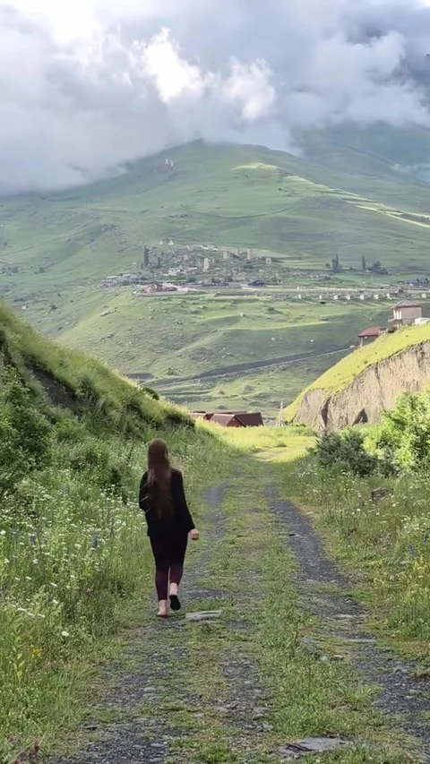 Woman Walking on Mountain Path Toward Village and Clouds Video stock 342265329