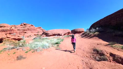 Woman walking toward camera on exploration path walking among deep red stone Stock Footage 328423643