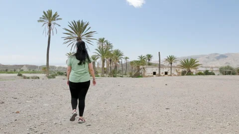 Woman Walking Toward Palm Trees and Abandoned Building in Tabernas Desert, Spain Video stock 309082353