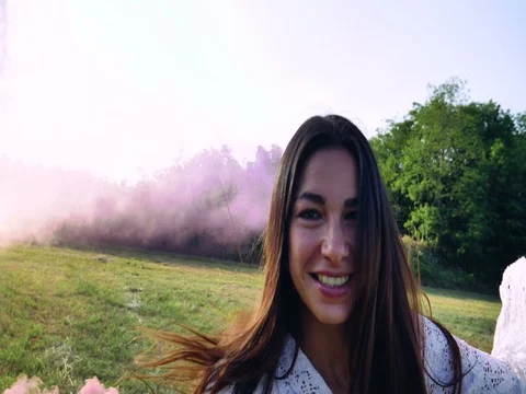 A woman walks across the field with a colored smoke flare in a white dress Stock Footage