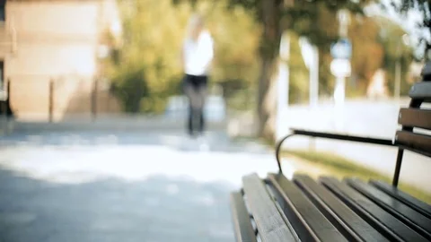 Woman walks in the defocused are go into focus zone sits down on bench uses Stock Footage