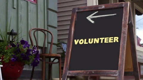 Woman walks past a sign that reads Volunteer and points to small business Stock Footage