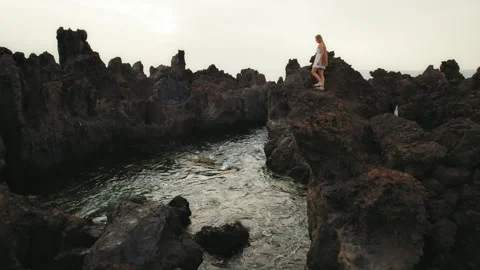Woman walks on rugged cliffs, surrounded by volcanic rock formations by the Stock Footage 306760853