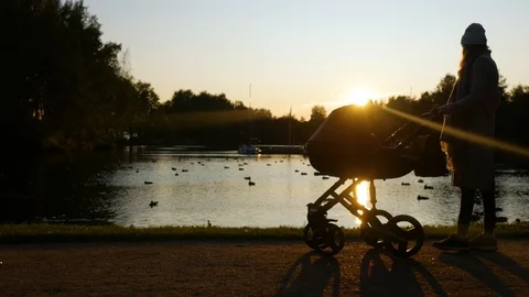 Woman walks with a stroller by the lake in the sunset Video stock 123671953